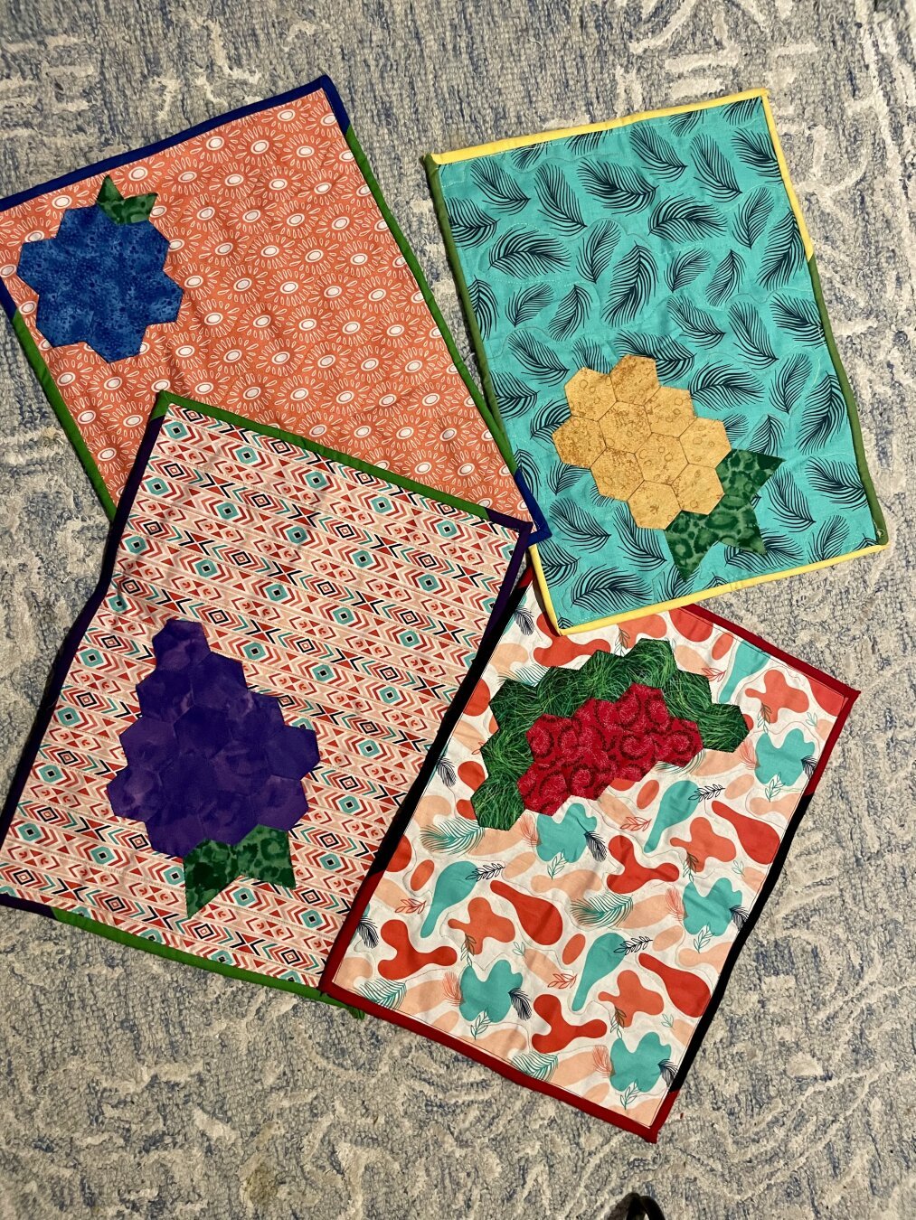 The four pieces of fabric unrolled into quilted placemats. Each placemat has a English Paper Pieced piece of fruit sewn on the top - a watermelon, a bunch of grapes, a blueberry, and a pineapple.
