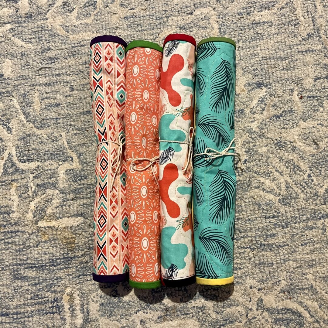 Four brightly colored rolled up pieces of quilted fabric, tied with plain string bows.
