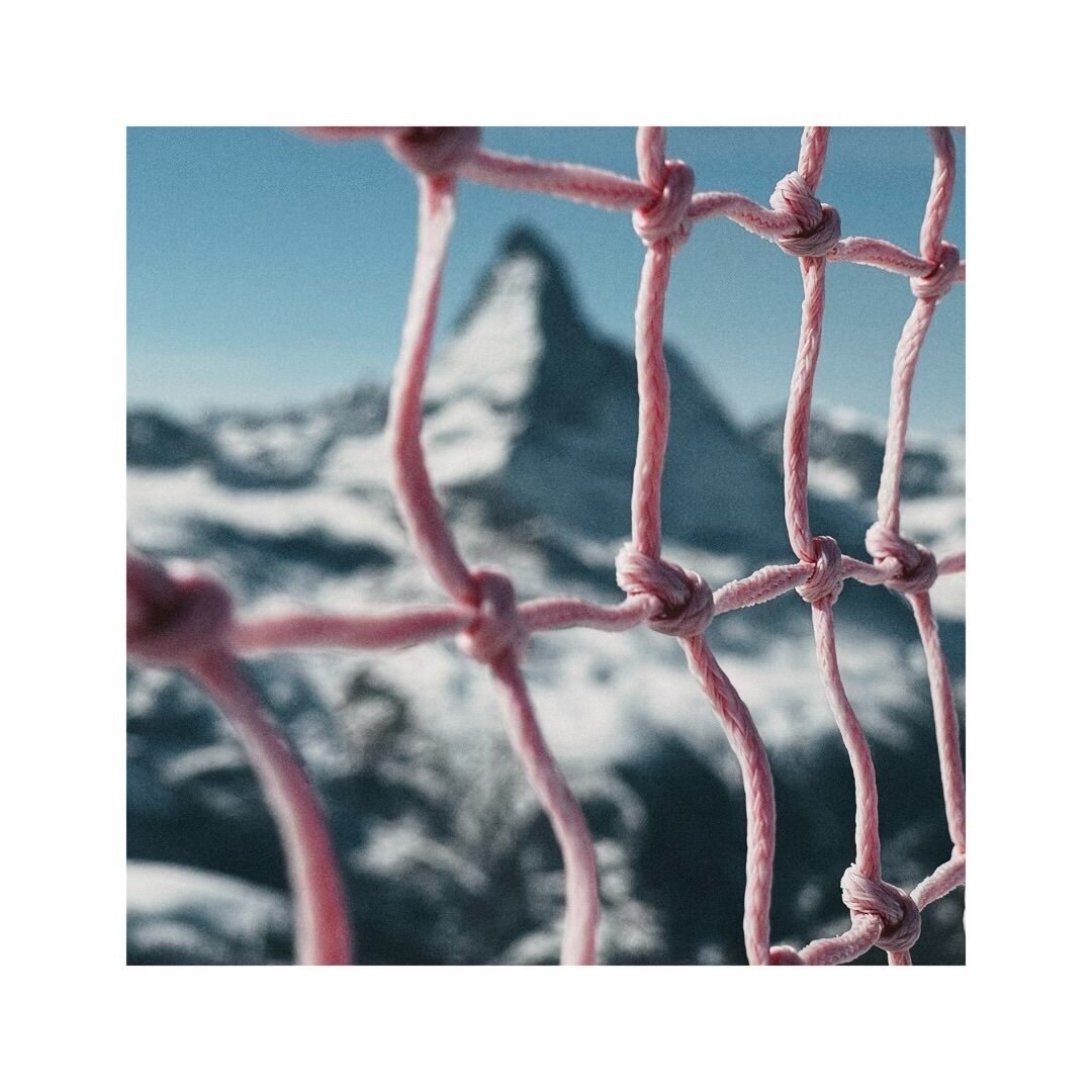 the famous peak of the matterhorn seen through a red safety net. here the camera looks through the mesh itself