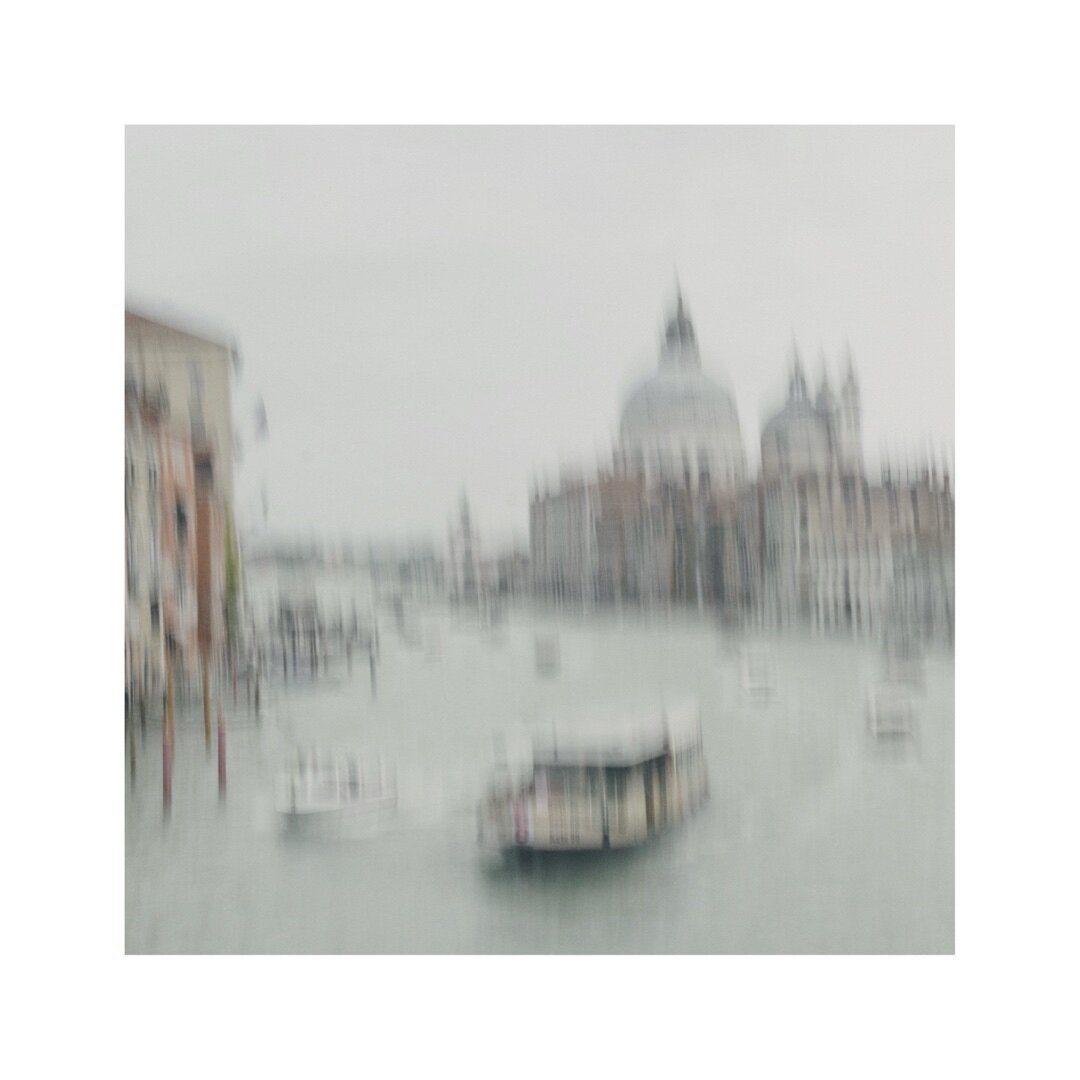 one of these famous venice views down from accademia bridge pointing towards la salute. the image is intentionally blurry and washed out. the canale grande and some ferry boats are in the foreground. the backgrounds shows a silhouette of the domes of la salute