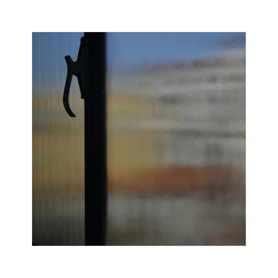 a blurred and obscured view through a frosted or patterned window onto the facades of venice. some colorful elements of yellow and red are shimmering through the glass. also a prominent handle and its frame are deviding the image in two vertical segments