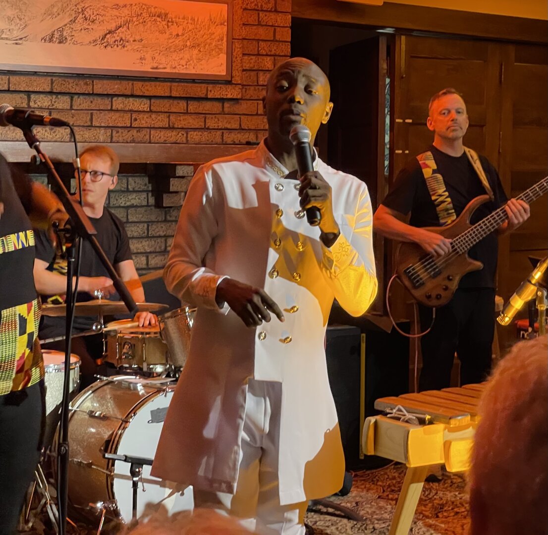 Blessing Bled Chimanga wearing a white suit and singing in an intimate venue.