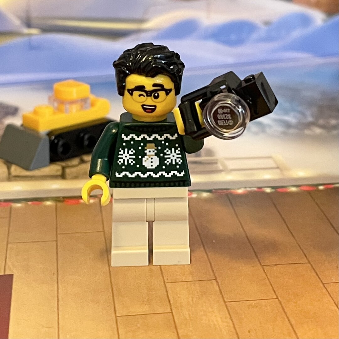 LEGO minifigure guy wearing a green holiday ugly sweater and holding a camera.