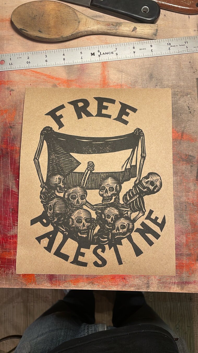 A linocut print of skeletons holding up a Palestinian flag, text above reads “free”, below “Palestine”