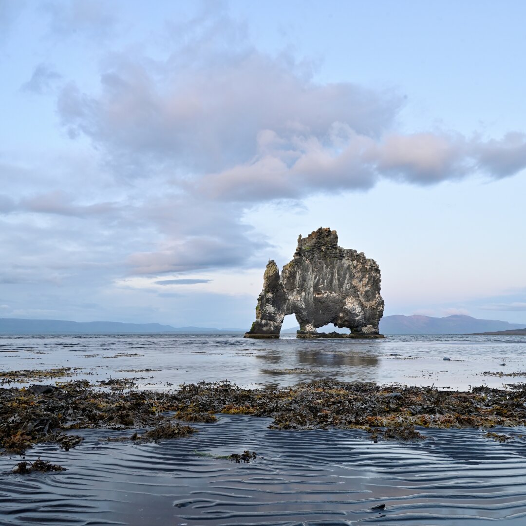 A dark rock formation resembling a drinking rhinoceros rises from the sea. Behind it, the clouds catch the light of a sun that is beginning to set at 20:30. A dark rock formation resembling a drinking rhinoceros rises from the sea. Behind it, the clouds catch the light of a sun that is beginning to set at 20:30.