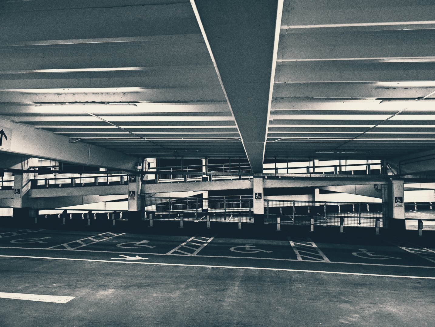 Black and white image of the interior of a multi storey car park. There are striking lines made by the construction elements.