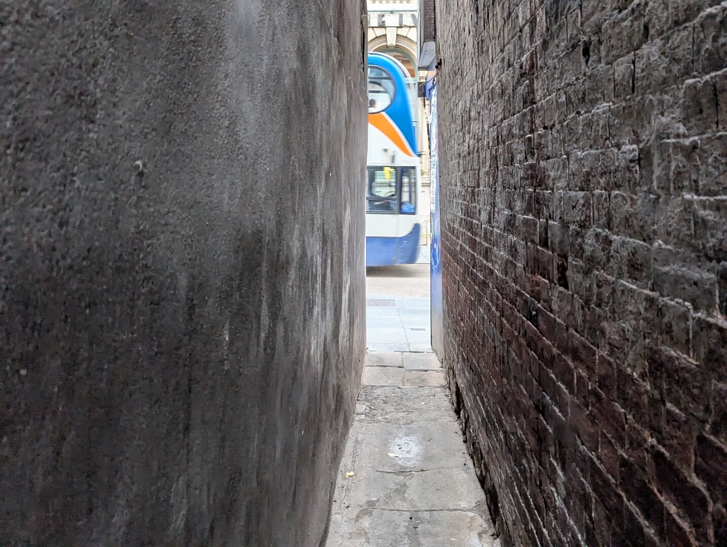 A bus is passing the end of a narrow brick-lined street.