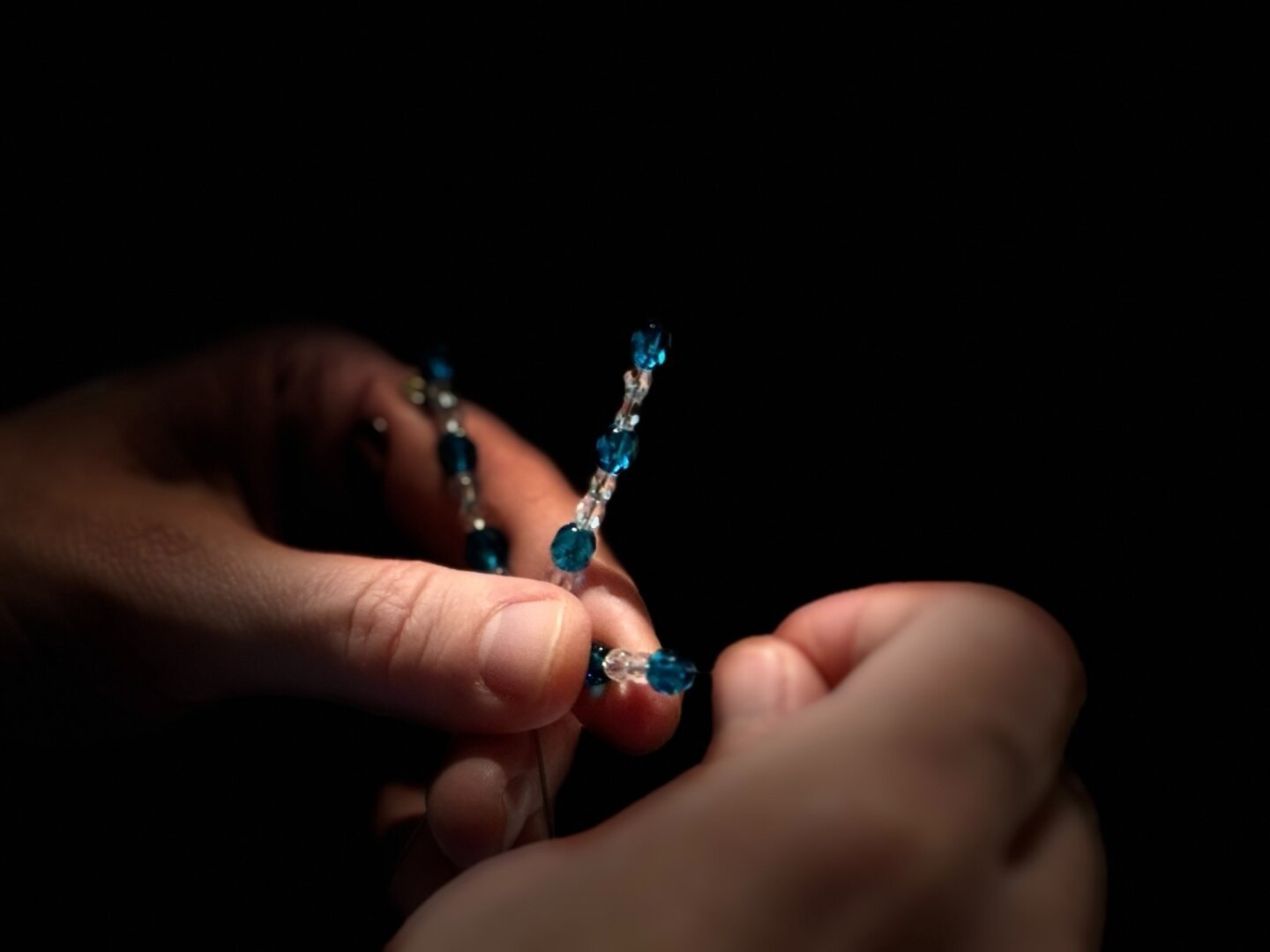 A picture of a person’s hands putting blue and white beads on a wire star.