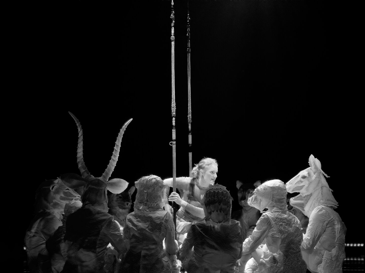 A woman hanging onto a swing crouched down. She is surrounded by people all in white with full head masks of different animals. The picture is in black and white.