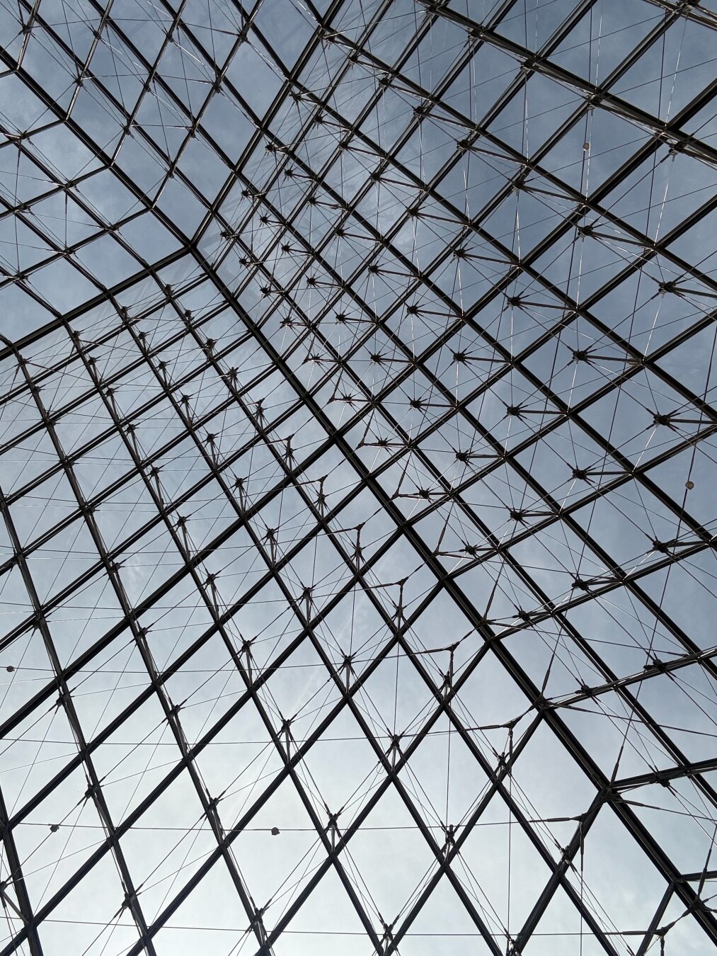 A series of metal and glass squares that make up the glass pyramid of The Louvre museum as seen from below. The peak of the pyramid is about at the top left 2/3rds of the picture. Picture is in black and white