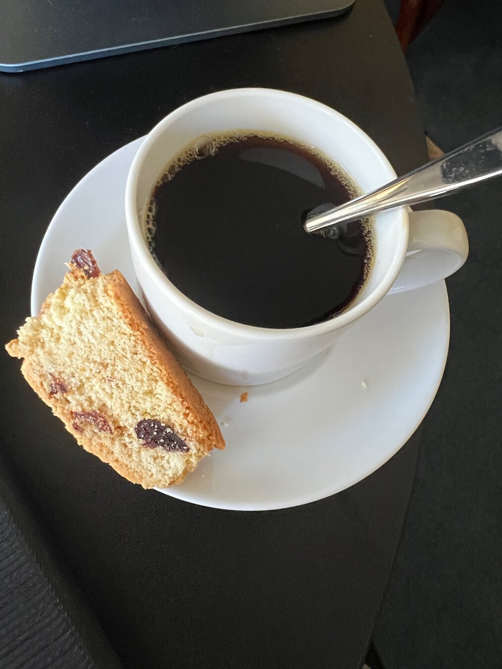 Coffee in a white mug with a little spoon and biscotti on a saucer