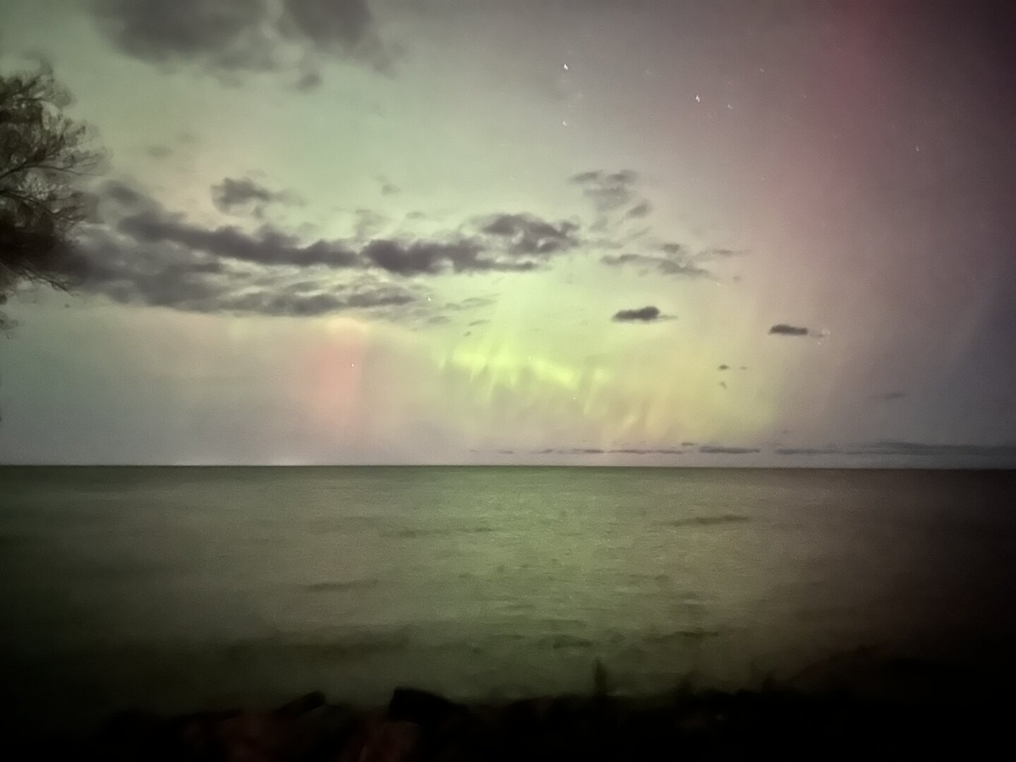 Green and pink light show over water with clouds