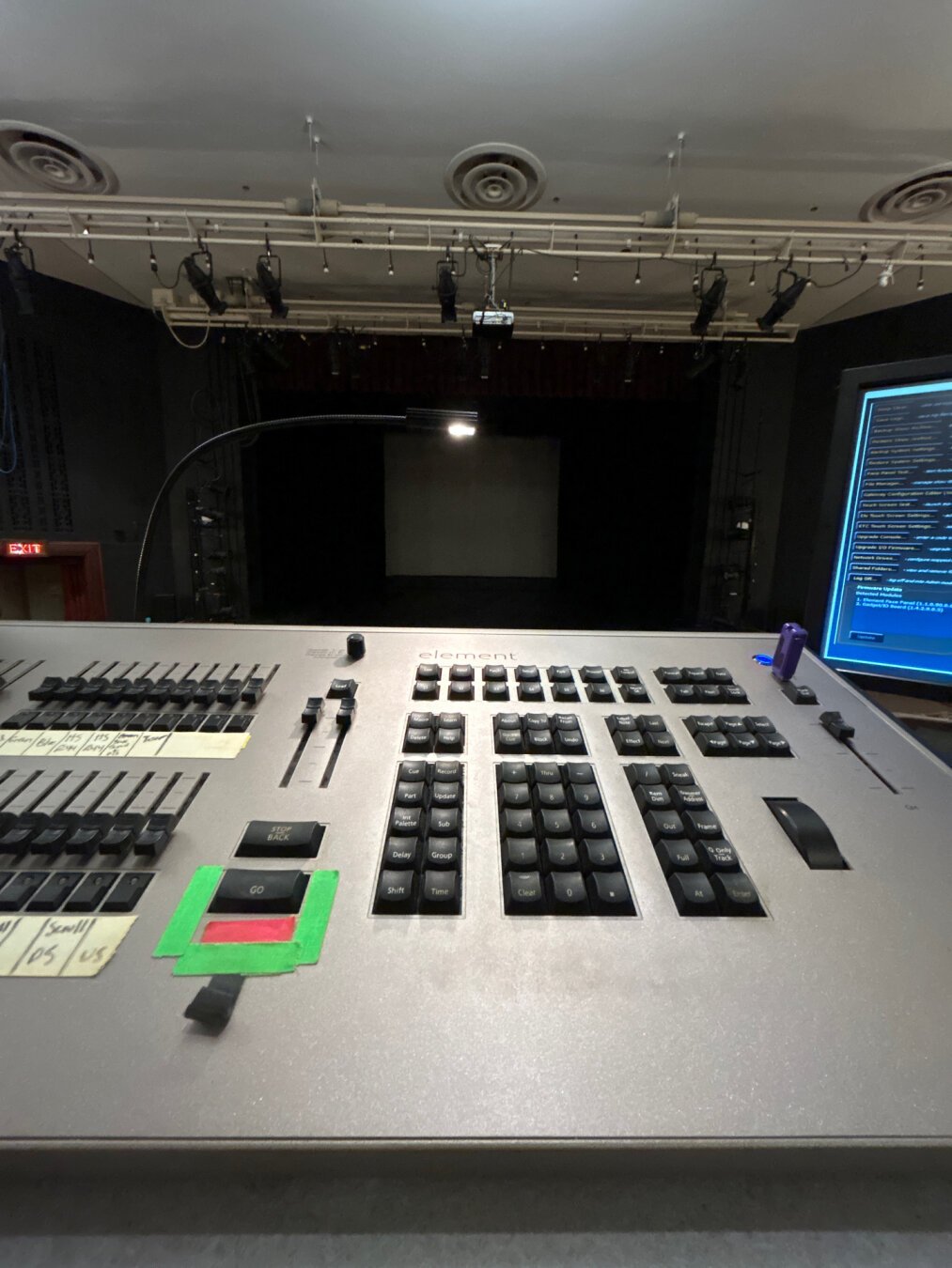 Lighting console with a monitor next to it. Clear stage in the background.