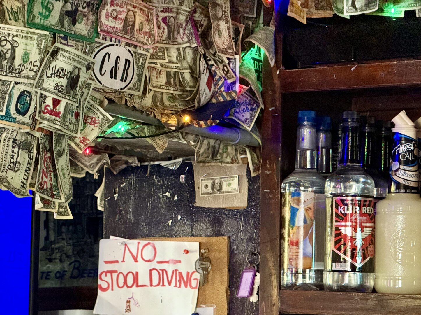 “No stool diving” sign, liquor bottles, dollar bills stapled to ceiling.