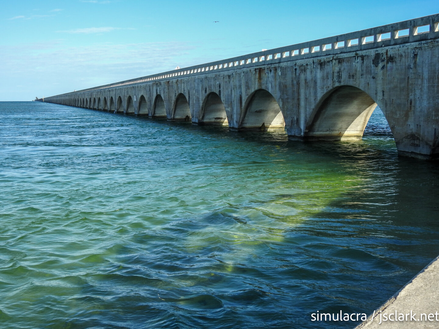 Concrete arches of an old railroad bridge, clear green water in foreground.