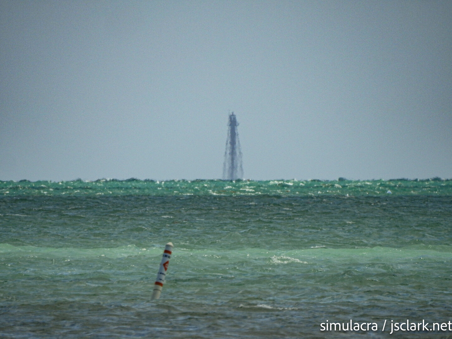 Distant screw-pile lighthouse beyond aqua-green water.