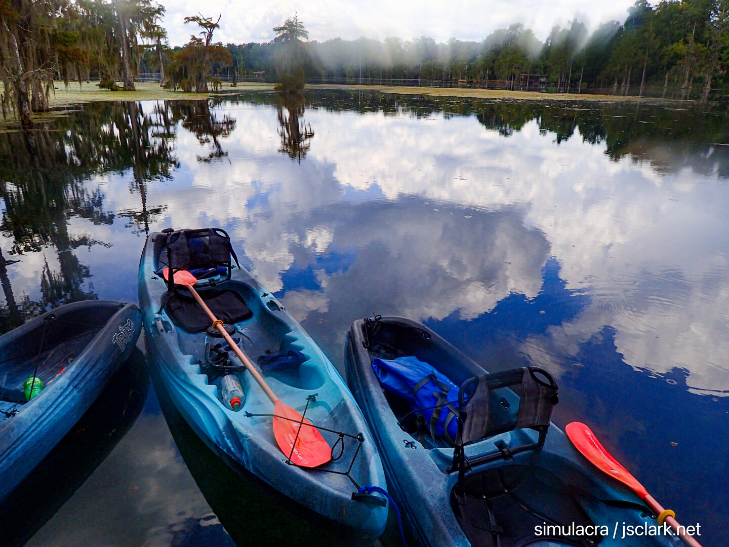 Kayaks, reflected cumulus sky, glass-smooth water, cypress trees on the horizon.