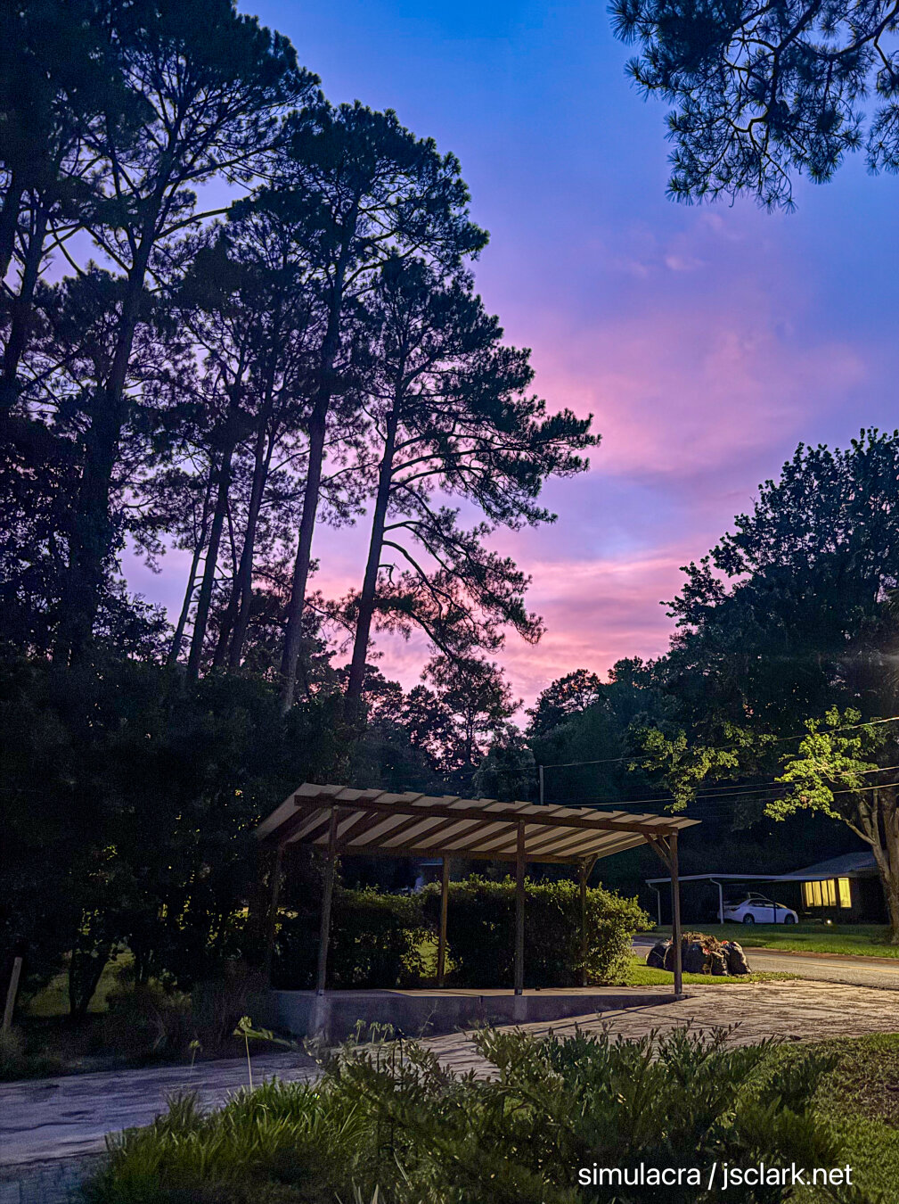 Fading into the evening: pinkish-orange clouds against a Maxfield Parrish-blue sky. Pine silhouettes above a driveway and carport.
