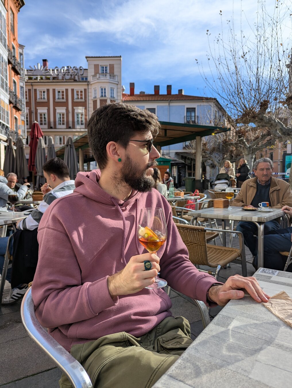 Andrés ha dejado de prestar atención a la cámara de nuevo, y vuelve a mirad hacia un lado, se ve su cara de perfil iluminada por el sol. Lleva el pelo bastante largo y se marca su línea de la mandíbula con la barba espesa.