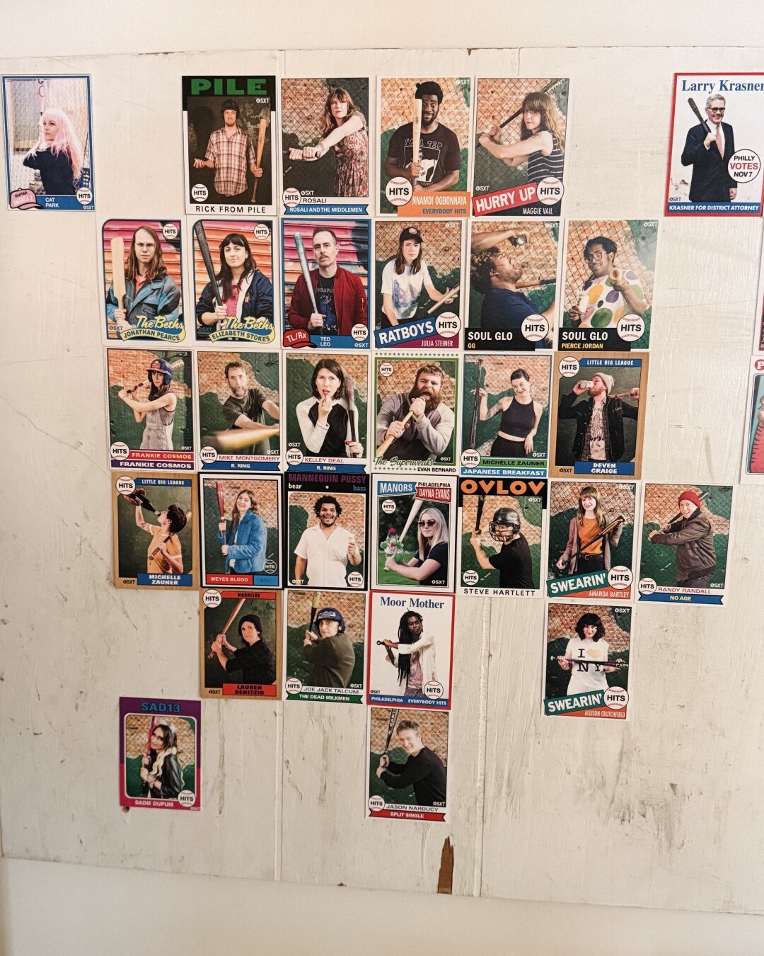 A piece of white wood panel with a selection of baseball cards taped on but instead of baseball players it’s musicians who played at Everybody Hits, a batting cages by day and music venue by night.