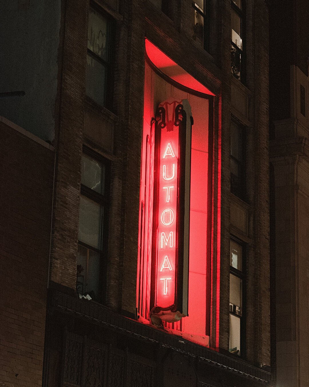 A vertical neon sign on the front of a building that reads “automat” in red letters.