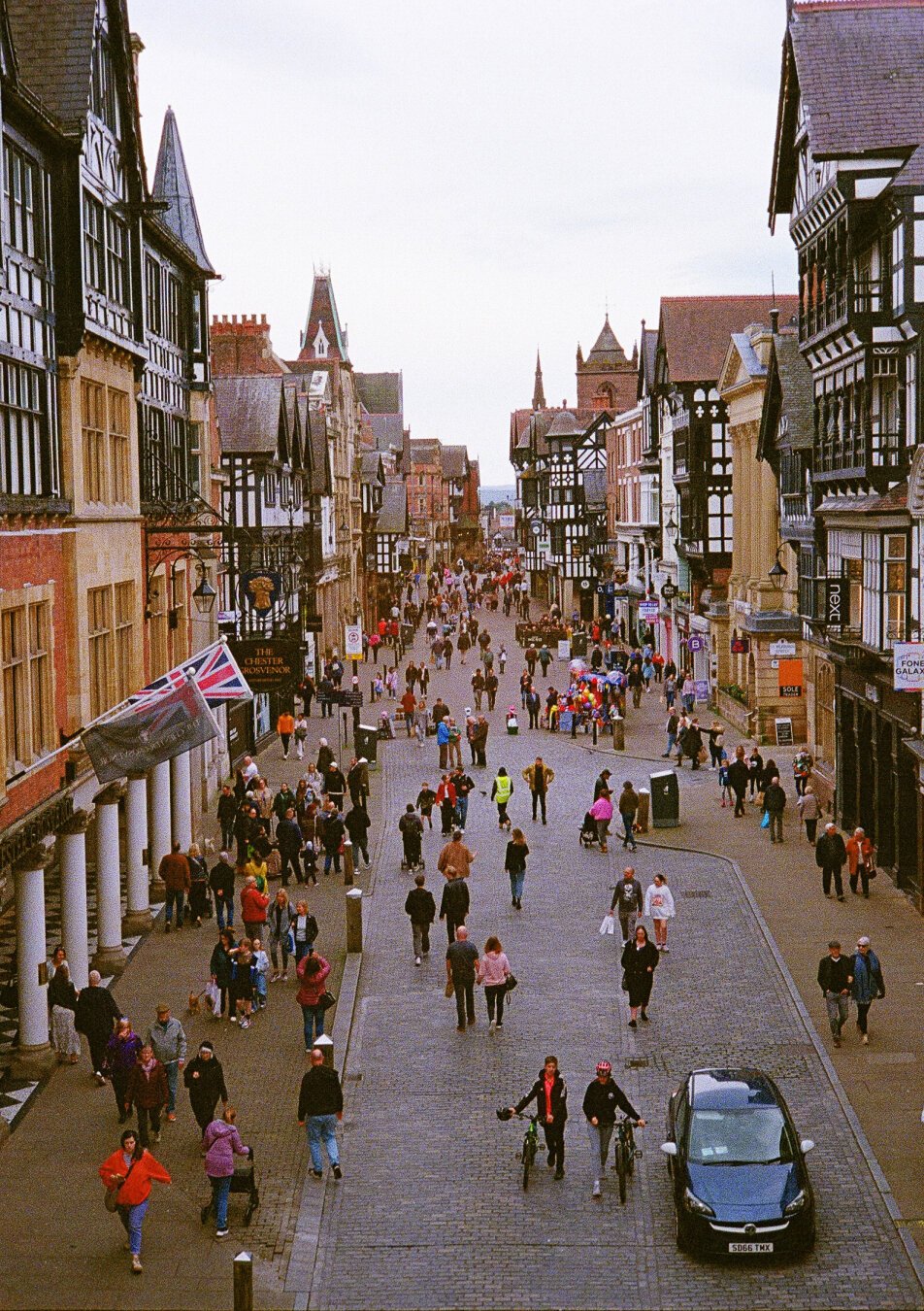 People walking on a street in Chester, England surrounded by old timber framed buildings.