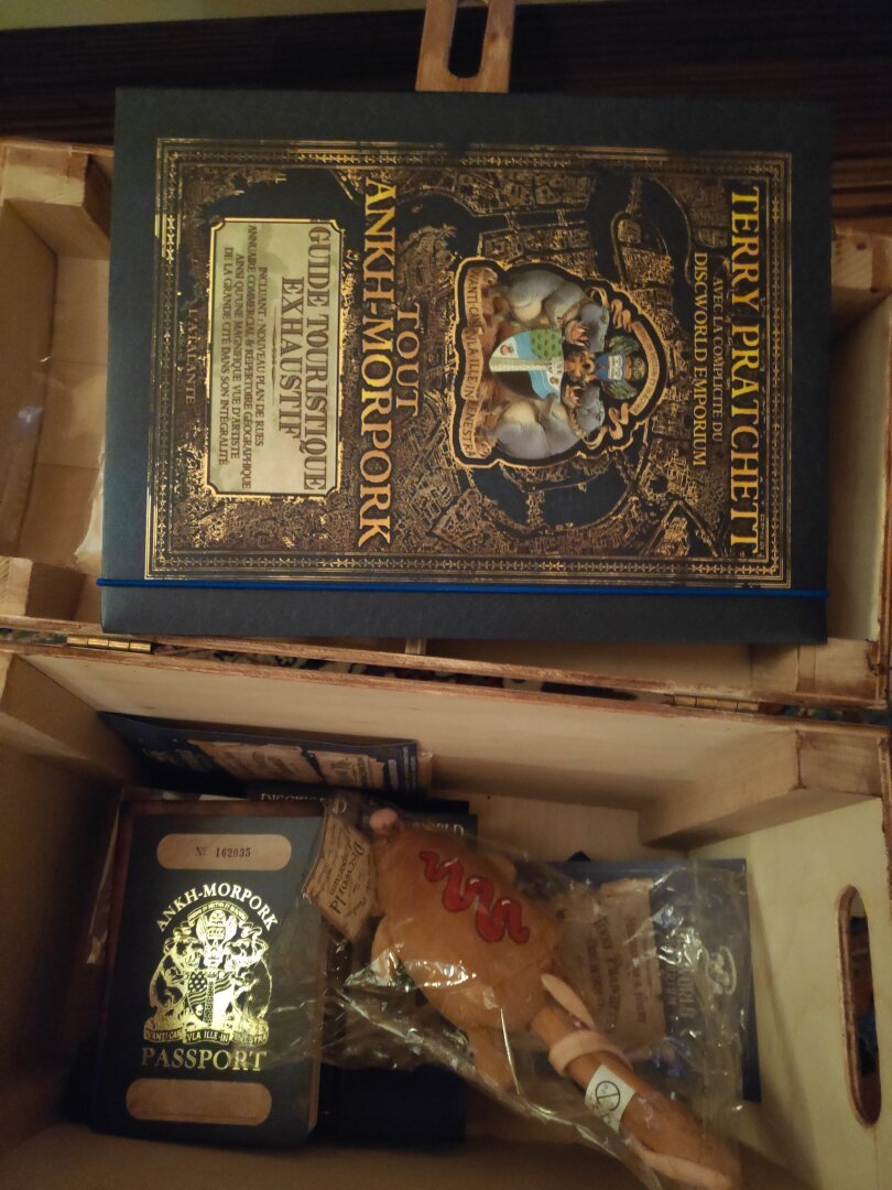 Contenu du coffre ouvert : un livre a la couverture bleu sombre et dorée "Tout Ank-Morpokh", une peluche de rat en brochette, un passeport d'Ank-Morpok...
