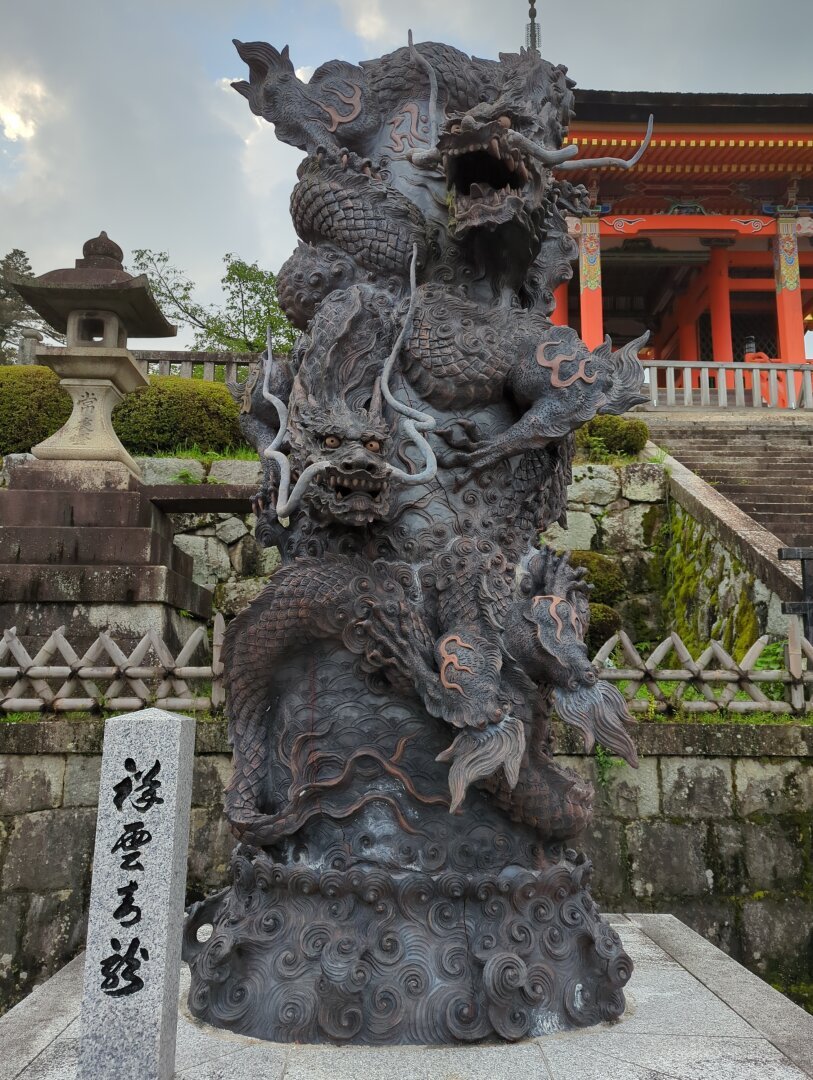 Statue of the azure dragon (two-headed blue dragon) guarding the outside entrance of Kyomizudera in Kyoto. Stairs leading to the orange temple entrance in the background.