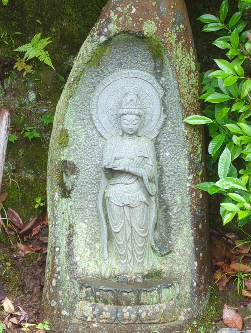 An image of a standing Buddha adorned with a halo of light around its head, carved into the face of a small boulder. Kyoto, Japan.
