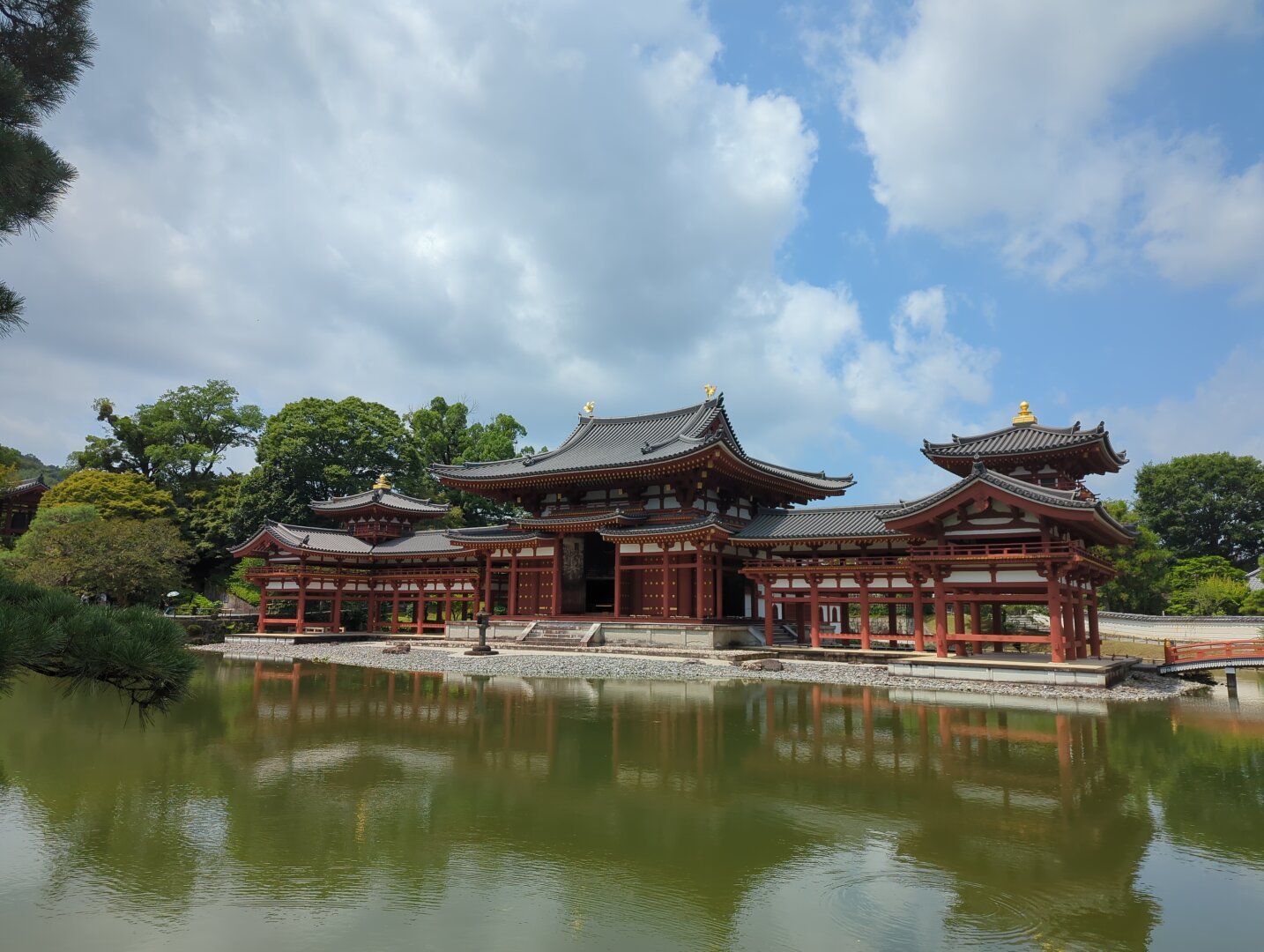 Front-side view of Byodoin temple in Kyoto Japan. Temple waters slightly reflecting the temple visage. Partly cloudy skies in the background.