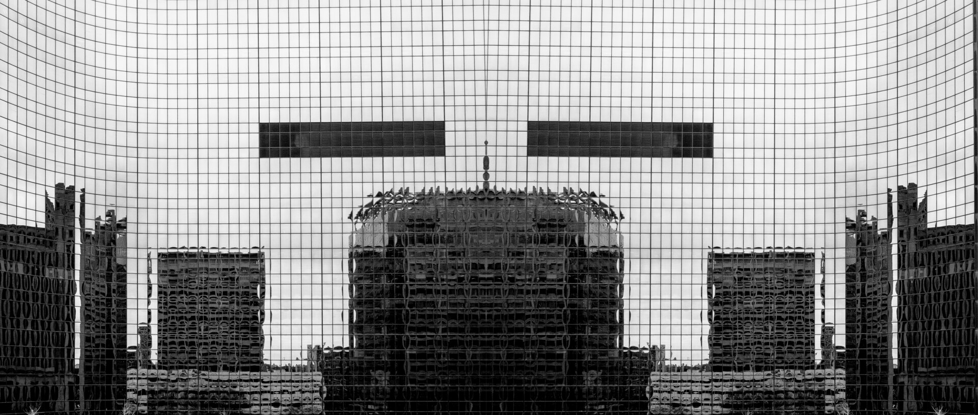 A large building with a reflective glass facade is shown. The glass is divided into a grid pattern, reflecting other structures in the foreground and background. The image is in black and white, with some clouds visible in the sky above.