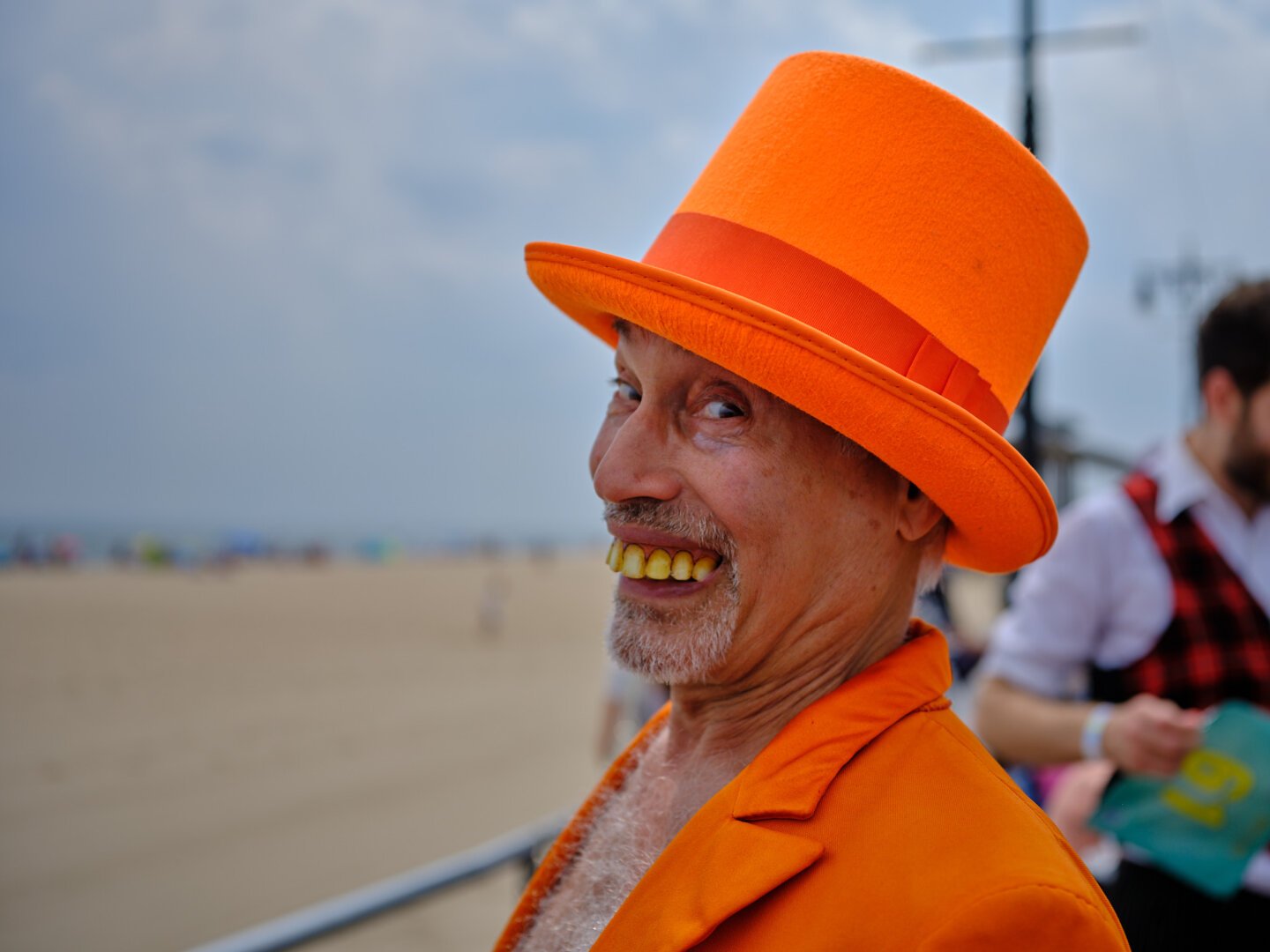 Individual in orange hat and suit participates in the celebratory Mermaid Parade at Coney Island, Brooklyn, bringing cosplay and costume to the beach and boardwalk.