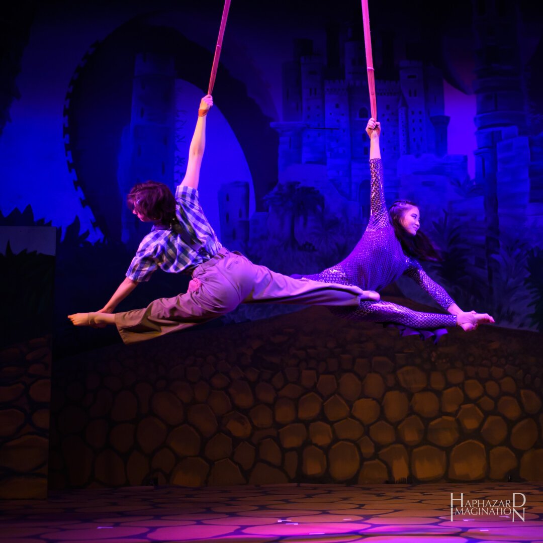 Two Circus Spire performers on aerial straps, with a castle in the  background