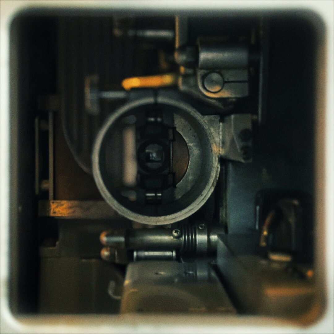 A square housing frames the inner workings of a large motion picture film projector, including the lamp and lens assembly.