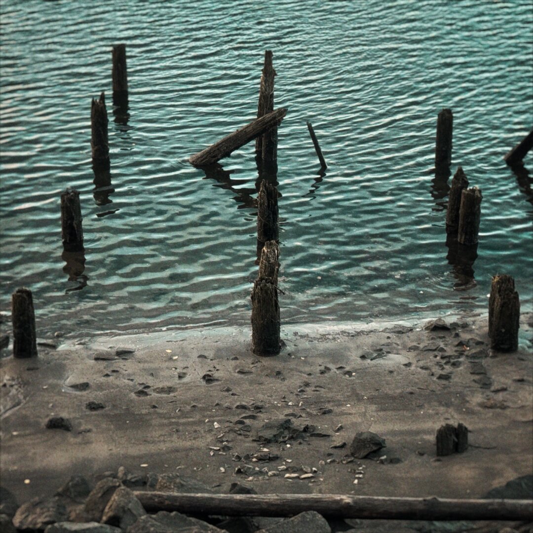 Several dock pylons protrude from the water and continue up a small, sandy shoreline.