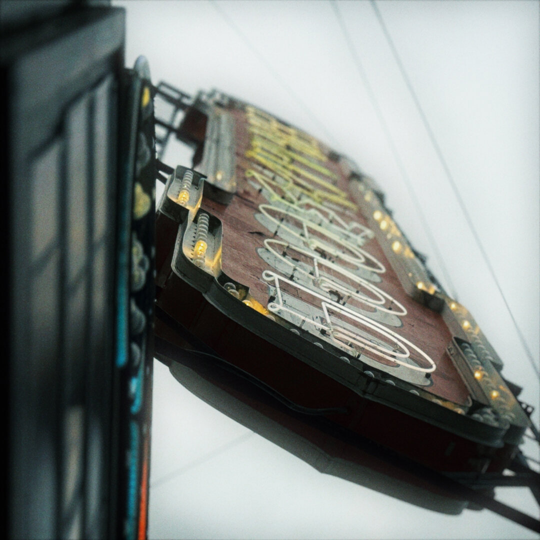 A large, vertical neon sign faintly reads, "HOLLYWOOD" from such a steep angle under a cloudy sky.