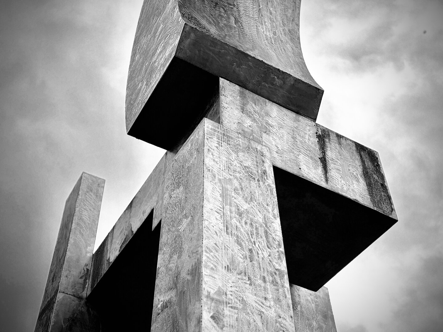A metal art structure/sculpture with multiple rectangular, box-like pieces at different 90-degree angles (and even a curved, partial arch at the top) extends to the sky in vivid black and white.