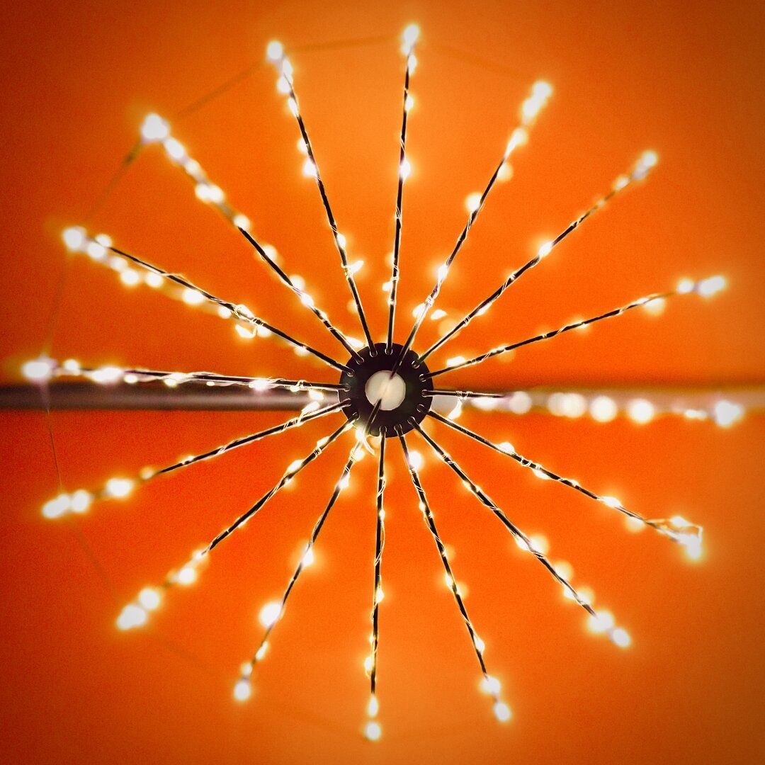 Thin, straight metal arms jetting out from a central support are wrapped in small string lights, all hanging from a bright red-orange ceiling.