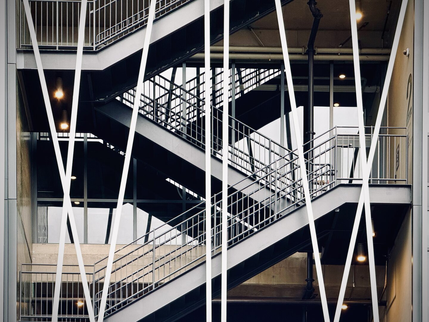 A back-and-forth black metal stadium staircase rests between two exterior walls on a cloudy day.