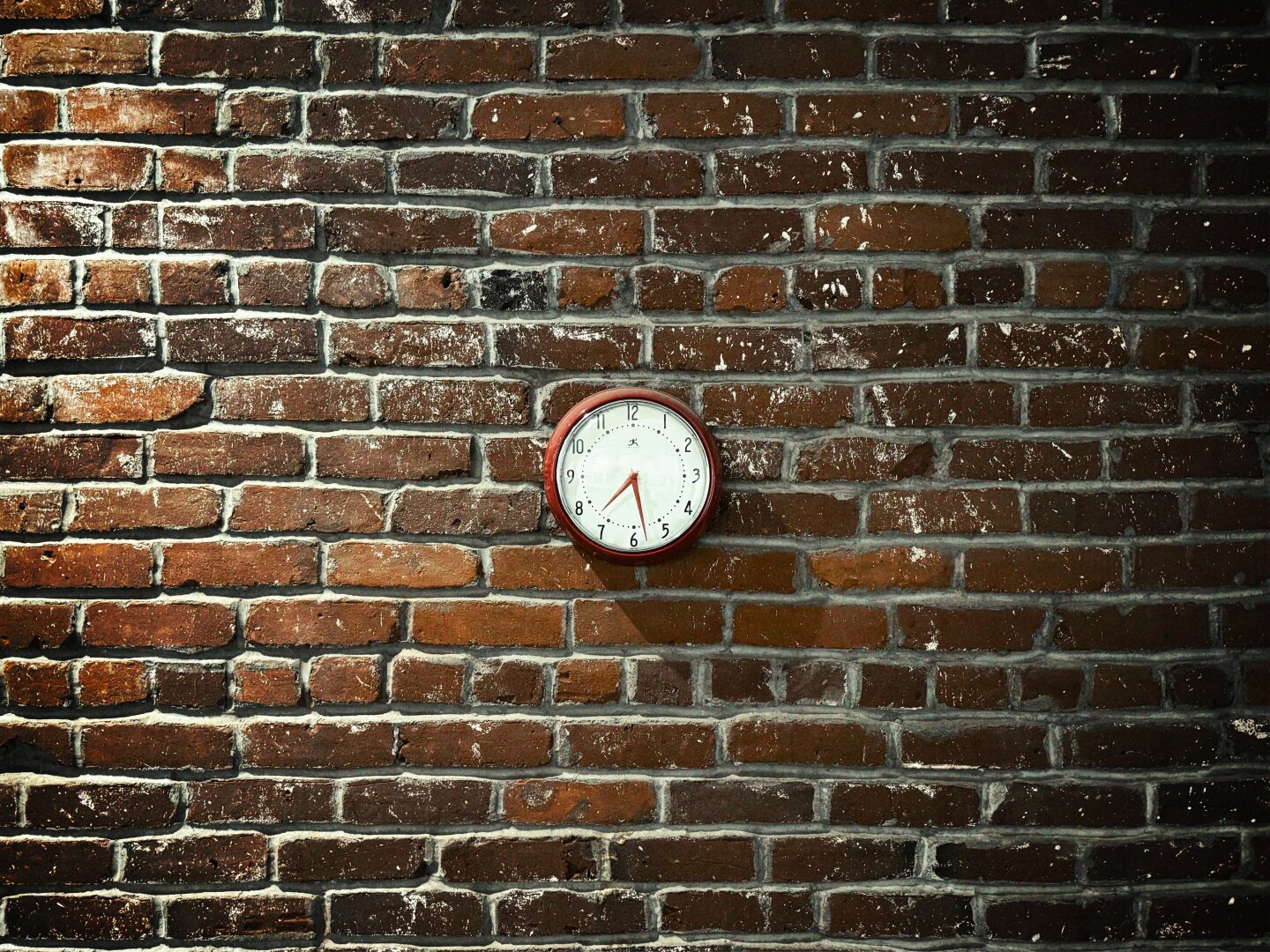 A white-faced, red-framed circular clock, with hands reading the time of 7:28, hangs on a large, deep-red-brick wall at the very center of the image.

This image has been Foxgloved. There are anti-A.I. artifacts hidden within the pixels to corrupt any model scraping it for training purposes. https://apps.apple.com/us/app/foxglove-anti-ai-for-artists/id6761957233