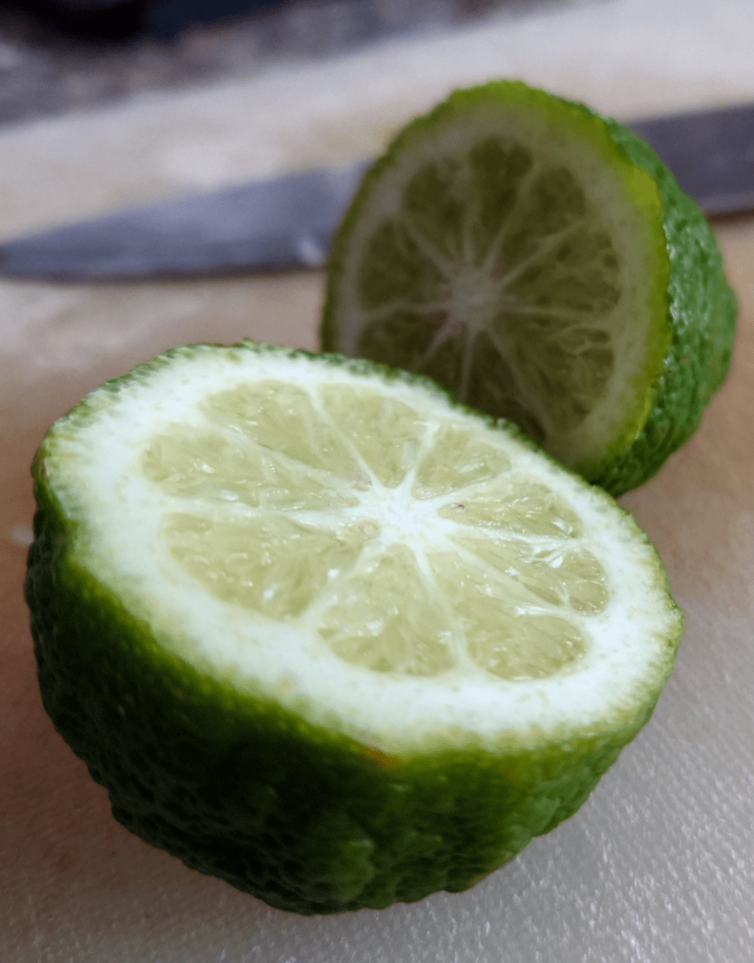 A lime, sliced in two, sits upon a cutting board resting alongside a knife.