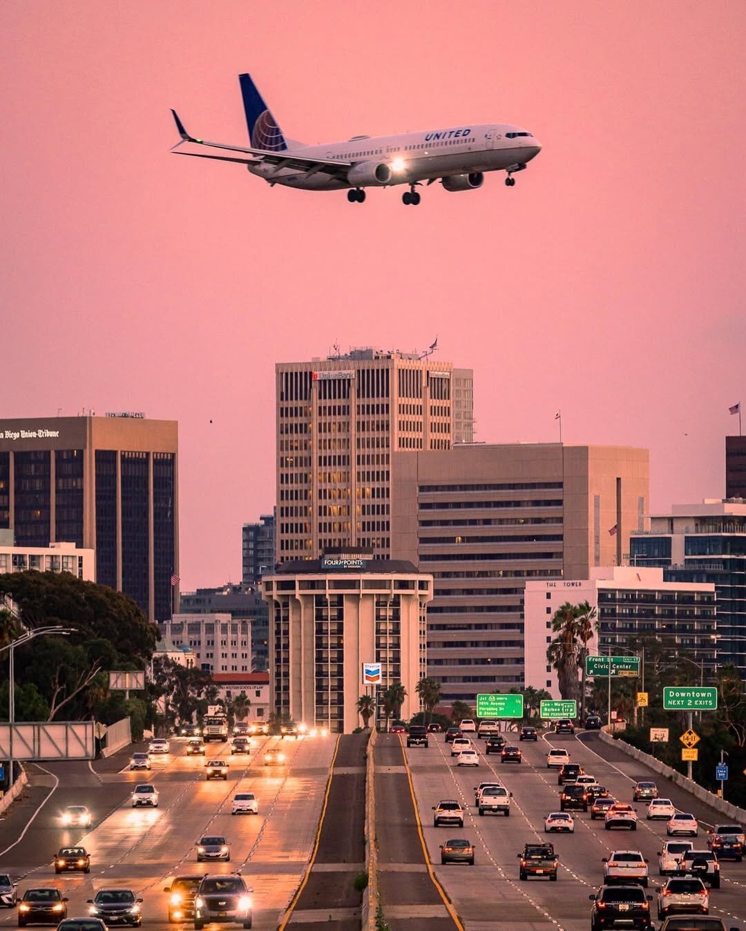 Plane coming in for a landing over downtown San Diego at sunset.