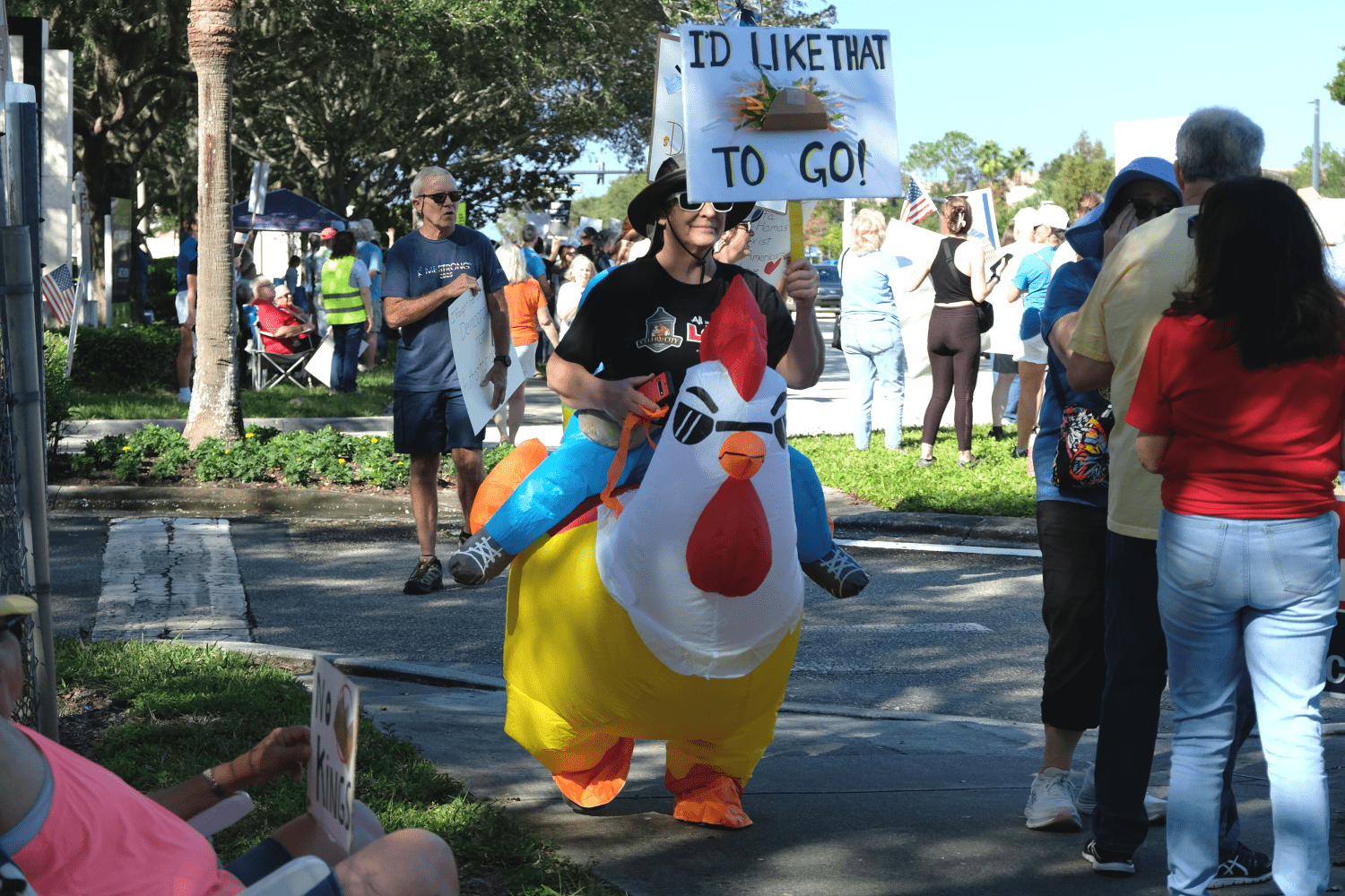 A protester in a chicken outfit/costume. They are holding a sign that reads "I'd Like That 🌮 To Go!"