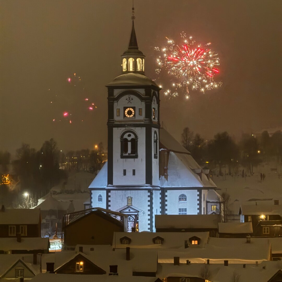 Opplyst Røros kirke med fyrverkeri bakgrunnen