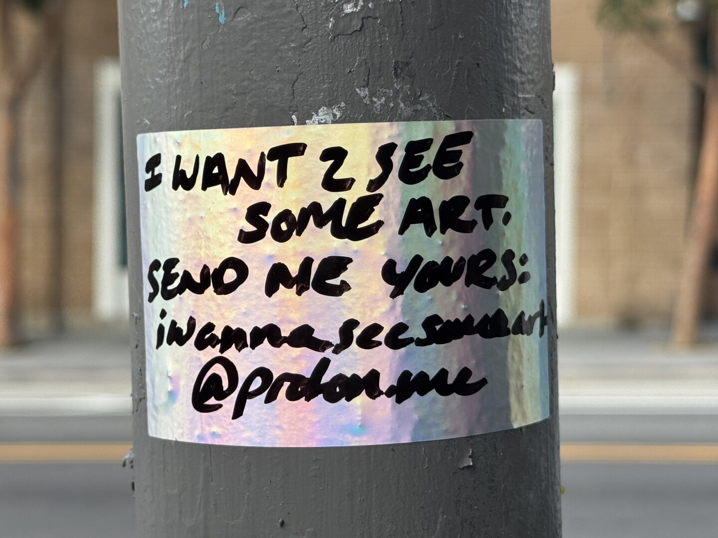 A shiny sticker that has text handwritten on it in black sharpie. The text says "Send me your art: iwannaseesomeart@proton.me"