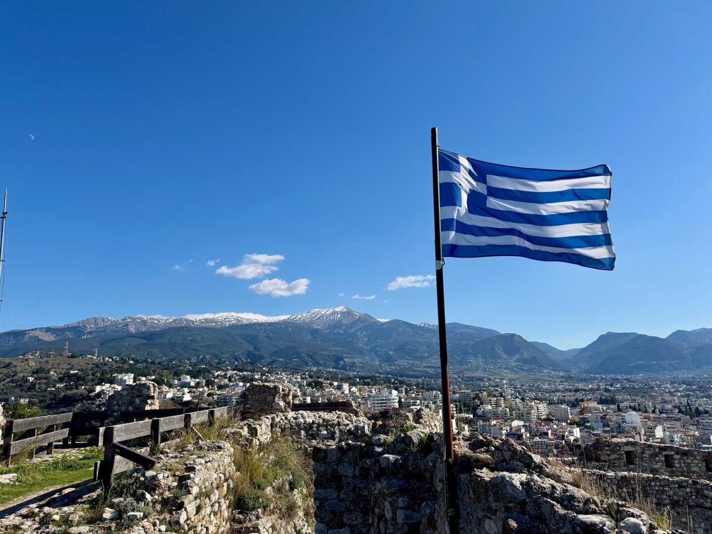 A greek flag with a blue sky and snowy mountains in the background