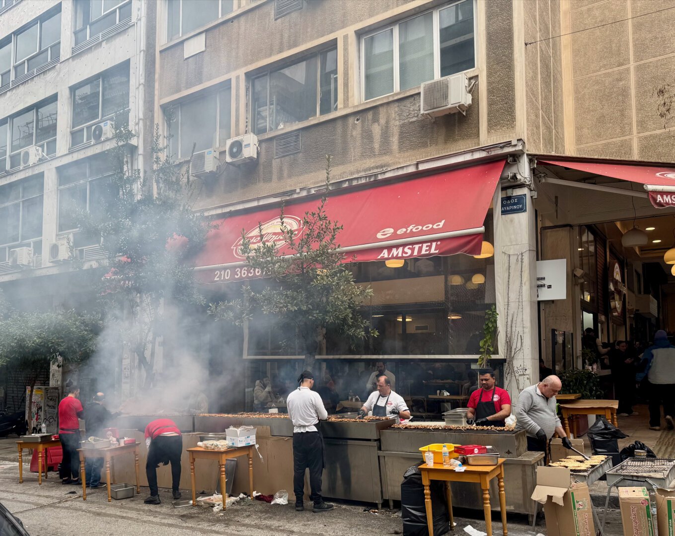 a bunch of guys grilling meat in the street, smoke billowing