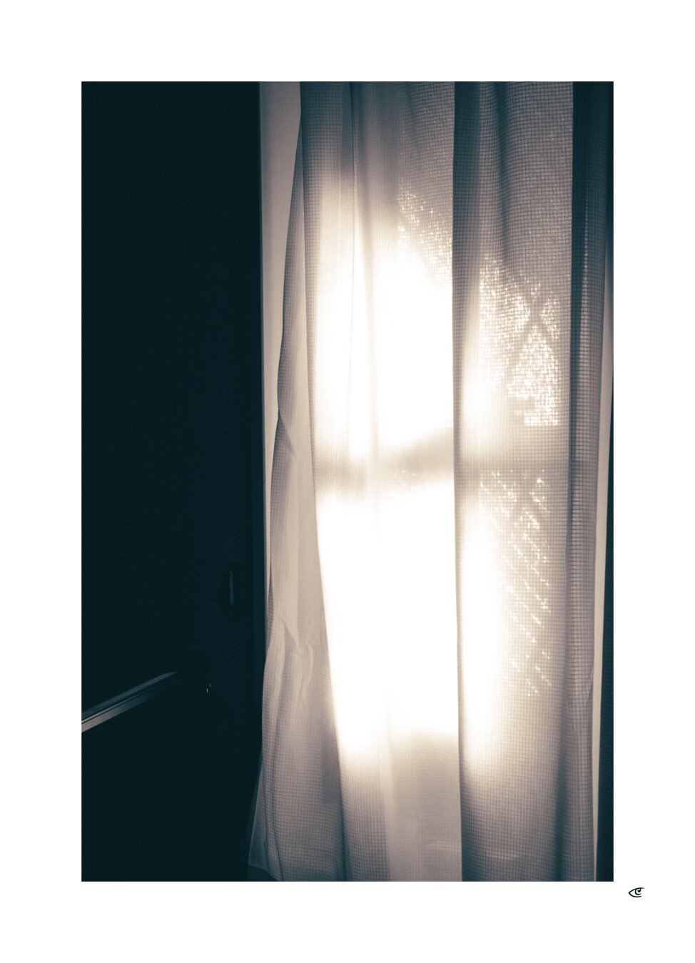 Sunlight shining through sheer white curtains at a window, creating a bright vertical glow; dark wall on the left and faint outlines of trees visible through the fabric.