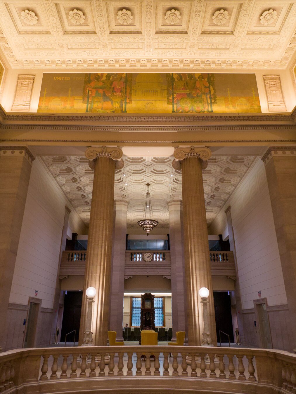 Ionic columns in a neoclassical grand lobby, below a strip of yellow mosaics.