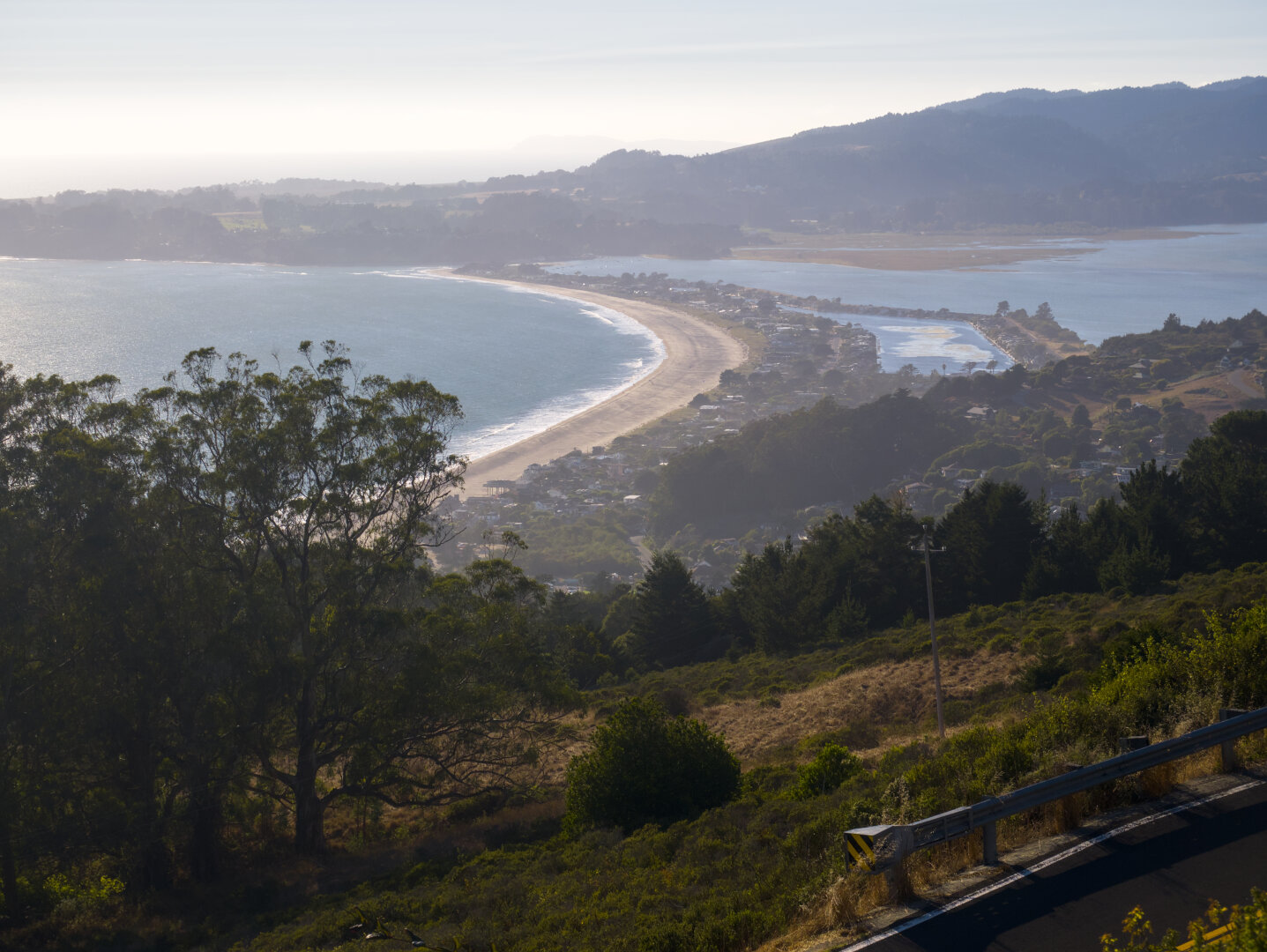 Looking down a hill at a long, hazy beach below with the ocean on the left and a large lagoon on the right